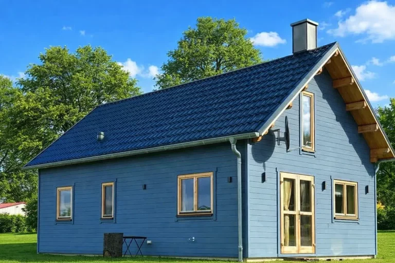 Ferienhaus Nordland Deluxe: Blaues Blockhaus mit dunklem Dach und grüner Umgebung. Ideal für Urlaub und Entspannung.