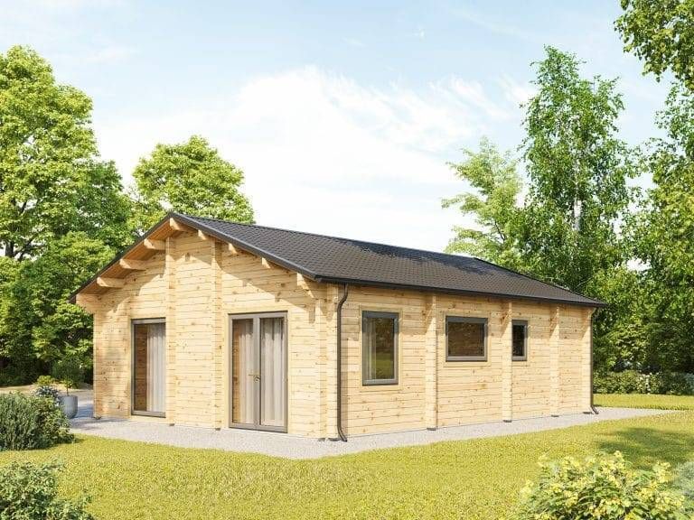 Blockhaus kaufen Ein kleines, einstöckiges Holzhaus mit schwarzem Dach steht auf einem Betonfundament. Es hat mehrere Fenster und eine Glastür. Das Haus ist von üppigem Grün und Bäumen unter einem klaren blauen Himmel umgeben.