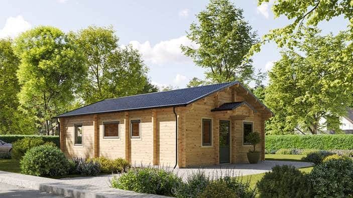 Ein kleines Holzhaus mit dunklem Dach steht in einer grünen Landschaft. Um das Haus herum sind Büsche und Bäume unter einem klaren Himmel. Das Haus hat mehrere Fenster und eine Eingangstür, die aus dem Bildwinkel sichtbar ist.