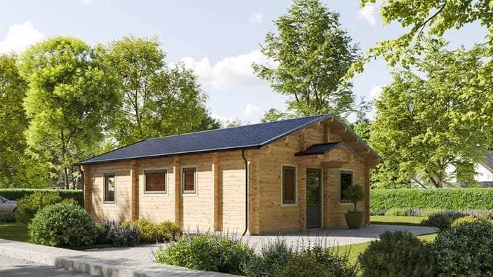 Ein kleines Holzhaus mit dunklem Dach steht in einer grünen Landschaft. Um das Haus herum sind Büsche und Bäume unter einem klaren Himmel. Das Haus hat mehrere Fenster und eine Eingangstür, die aus dem Bildwinkel sichtbar ist.