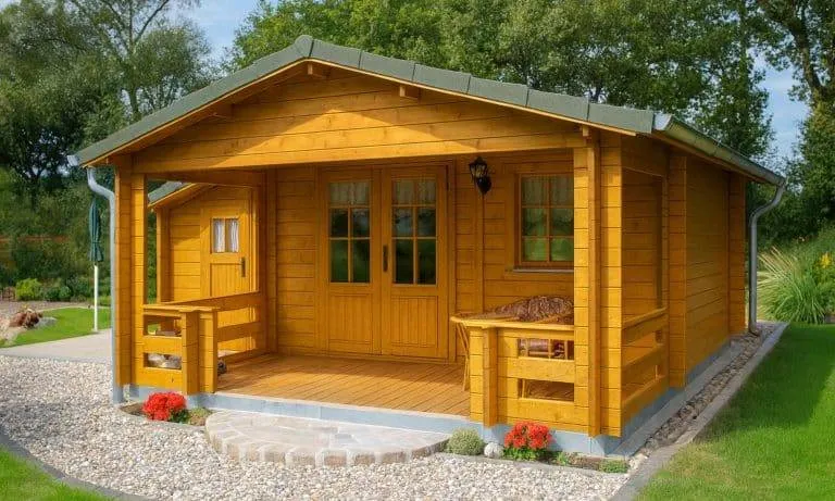 Eine kleine Holzhütte mit einer überdachten Veranda, Doppeltüren und Fenstern liegt an einem Steinweg, umgeben von Gras, Pflanzen und Bäumen. Rote Blumen sind in der Nähe der Eingangstreppe gepflanzt.